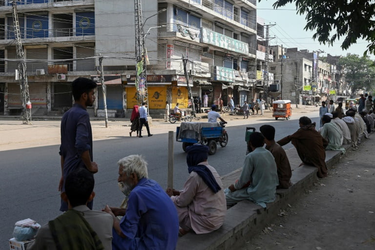Des ouvriers journaliers assis sur un trottoir près de magasins fermés lors d'une grève nationale des commerçants contre la hausse des prix et l'inflation, le 2 septembre 2023 à Lahore, au Pakistan (AFP - Arif ALI)